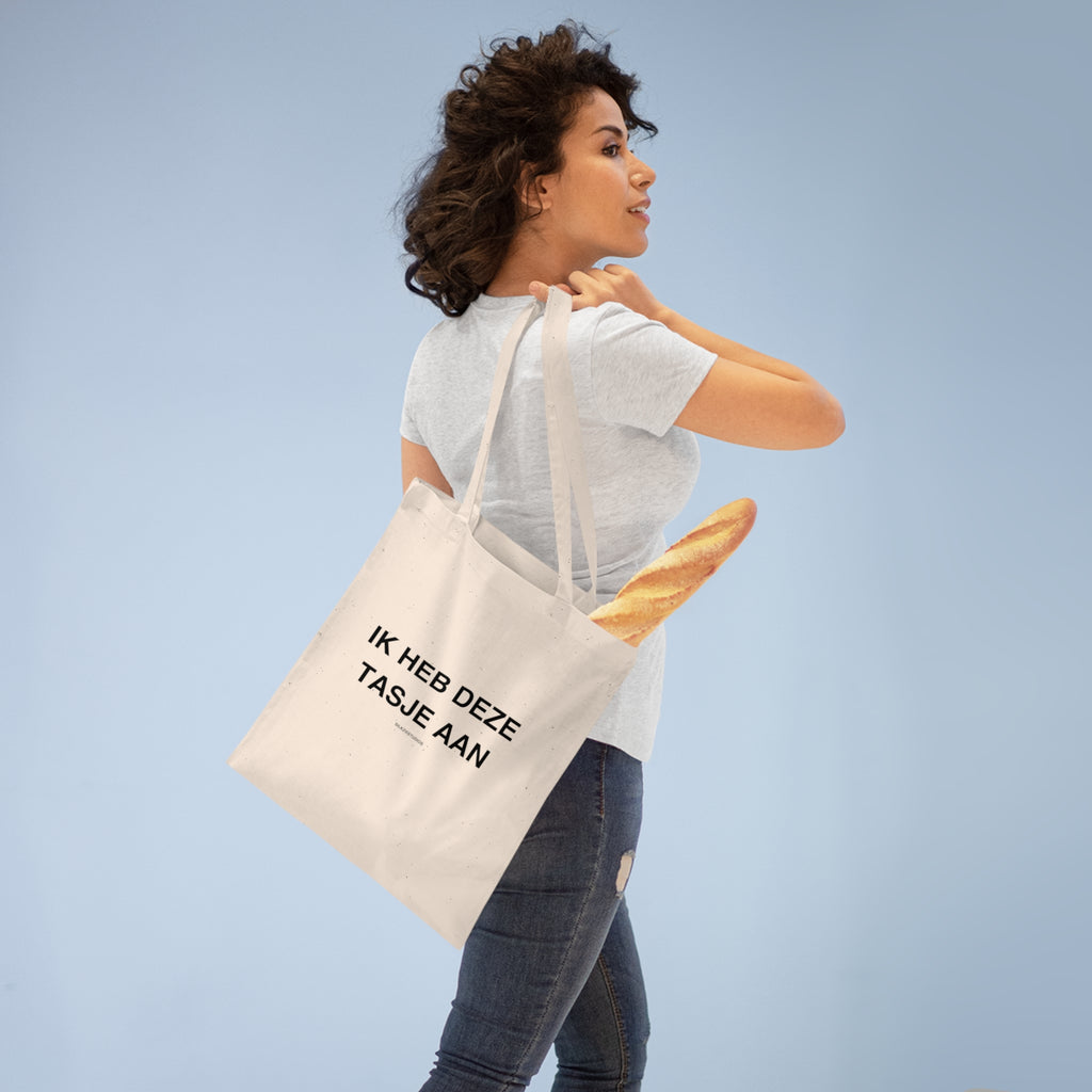 Vrouw draagt een tote bag met de tekst ik heb deze tasjes aan tote bag en een stokbrood